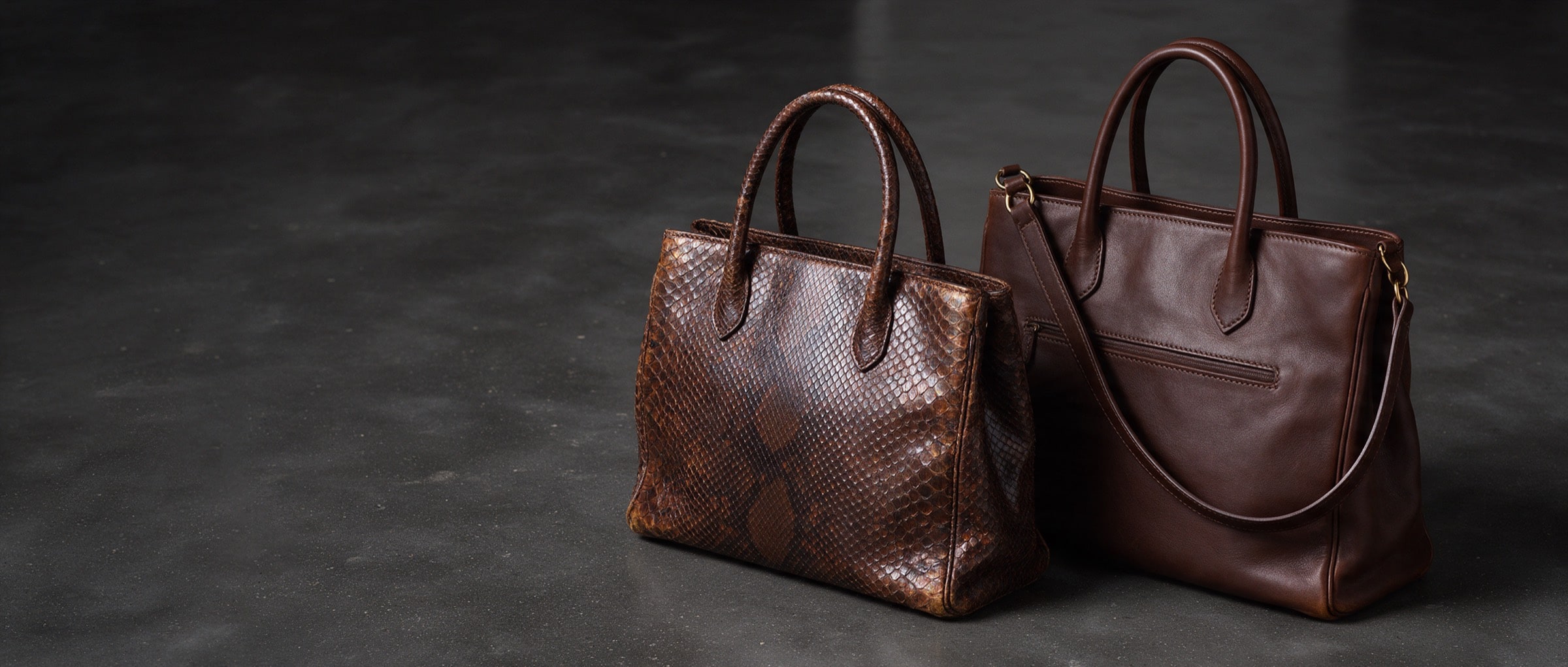 Two structured top-handle leather handbags, one exotic and one calfskin, on a black polished surface