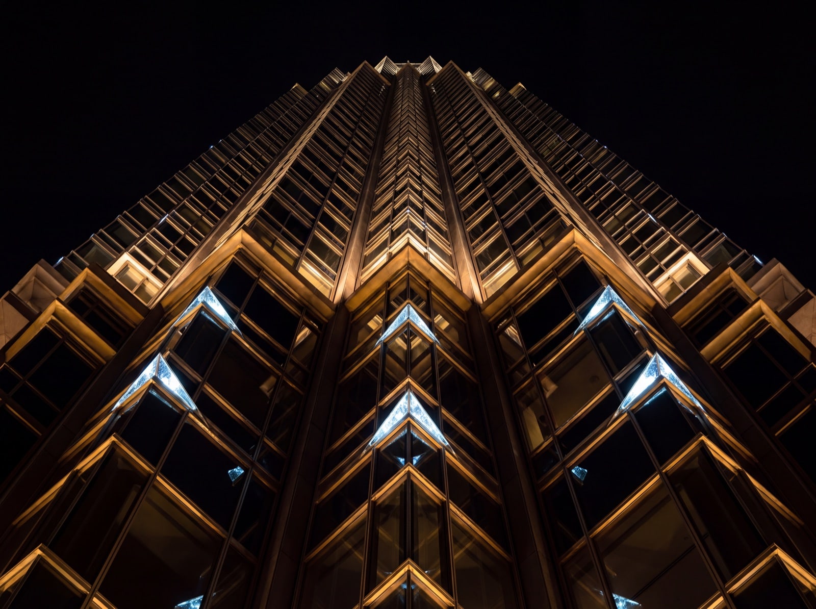 A modern glass tower at night seen from its base, facade catching warm gold interior light