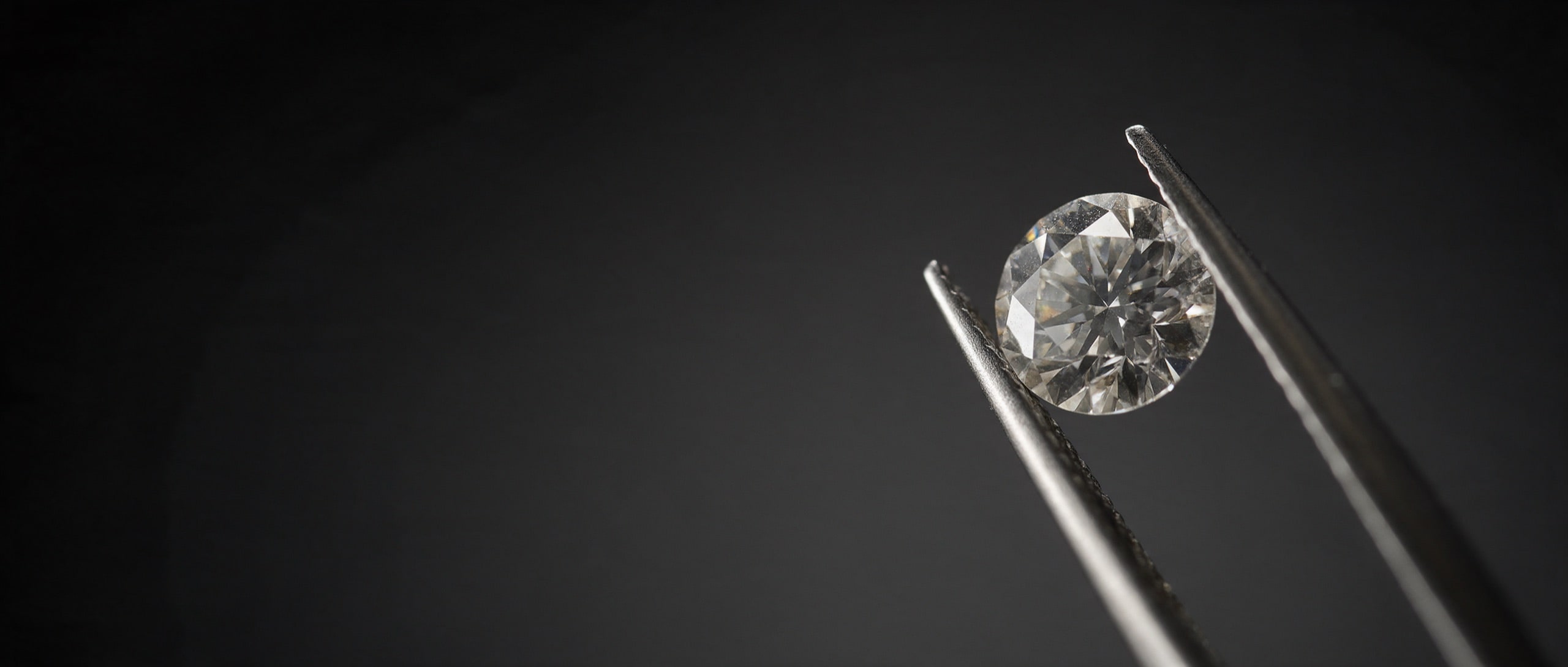 A round brilliant diamond held in polished tweezers against black